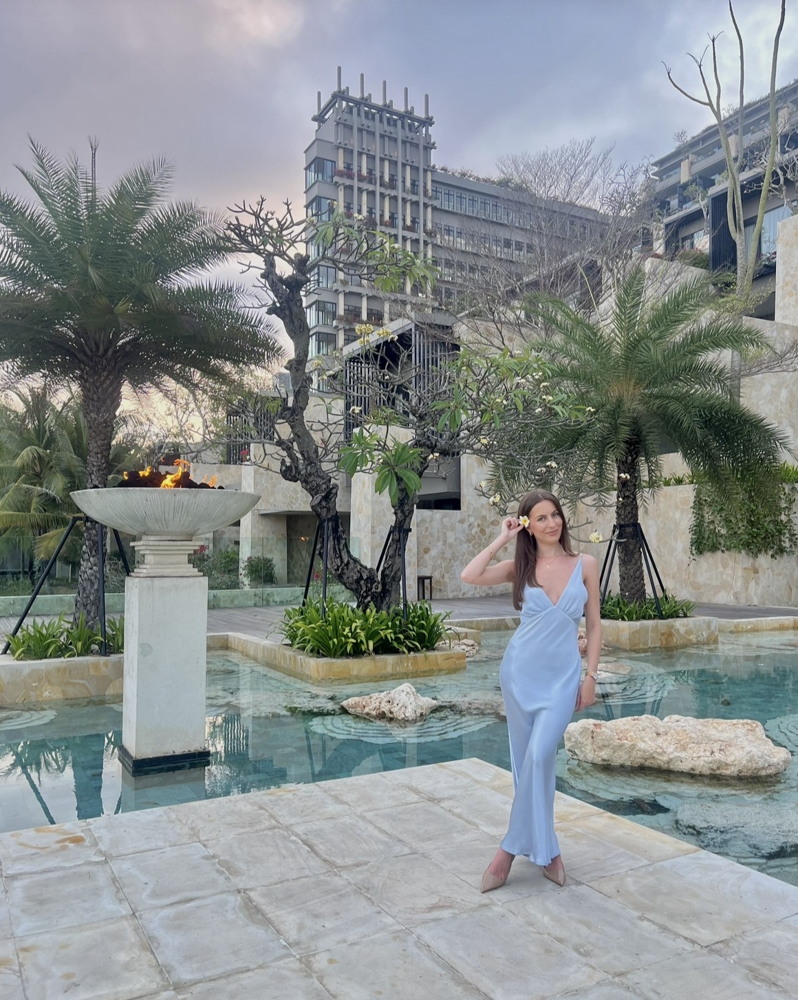 Woman in a blue slip dress by a resort water feature